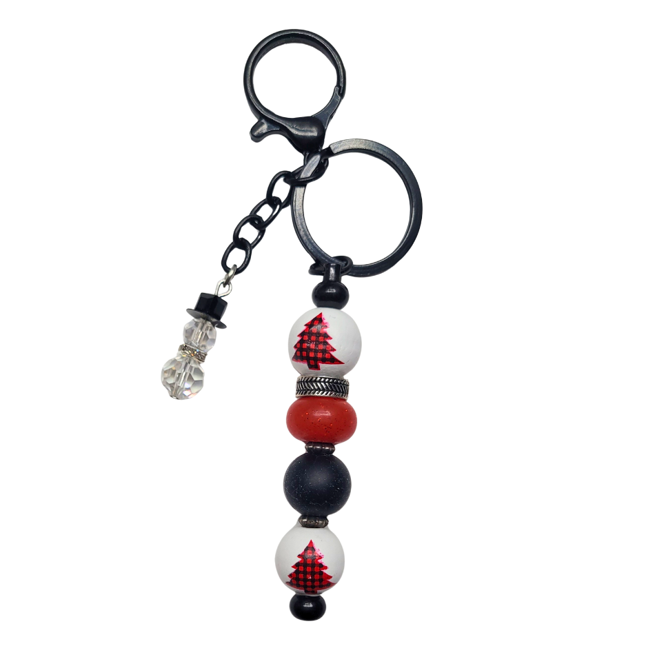 Handmade holiday charm with black hardware, featuring white beads painted with red and black plaid Christmas trees, a matte red bead, and a crystal snowman dangle.