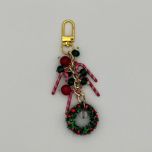 A richly textured, chunky handmade planner or purse charm featuring a cluster of traditional holiday elements. The charm includes red and dark green beads, three pink-striped candy cane charms, and a bright green tinsel-look foil wreath focal with red berry beads. It is attached to a gold-toned lobster clasp and chain.