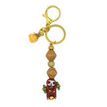 Load image into Gallery viewer, Tree Hugger Glimmer purse charm featuring a cute sloth focal bead hanging from a branch, with wood, crystal, and pale yellow beads.